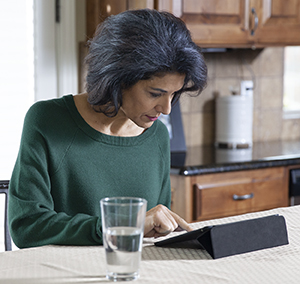 Mujer sentada junto a una mesa mirando una tableta electrónica.